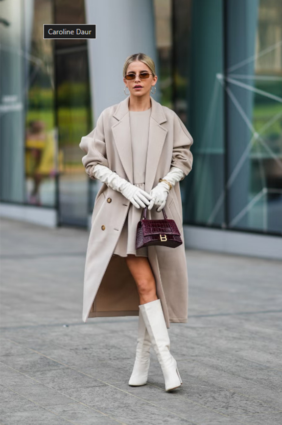 Blond dáma s uhladeným účesom v bézovom trenčkote s velkými glamour bézovými rukavicami stojaca pred budovou